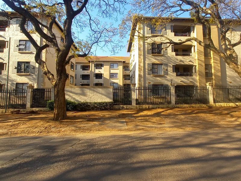 Street view of a multi-story apartment complex featuring balconies and secure perimeter fencing.