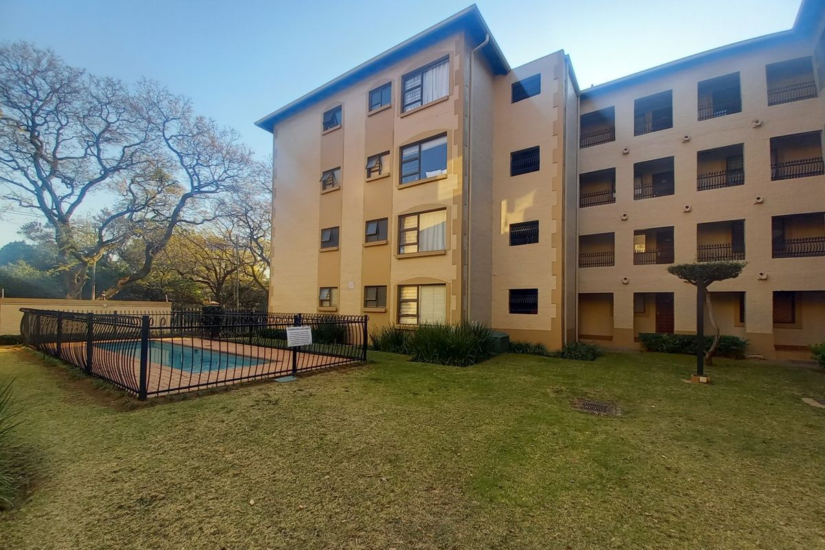 Exterior view of an apartment complex featuring a communal swimming pool, landscaped garden area, and multi-story building facade with balconies.