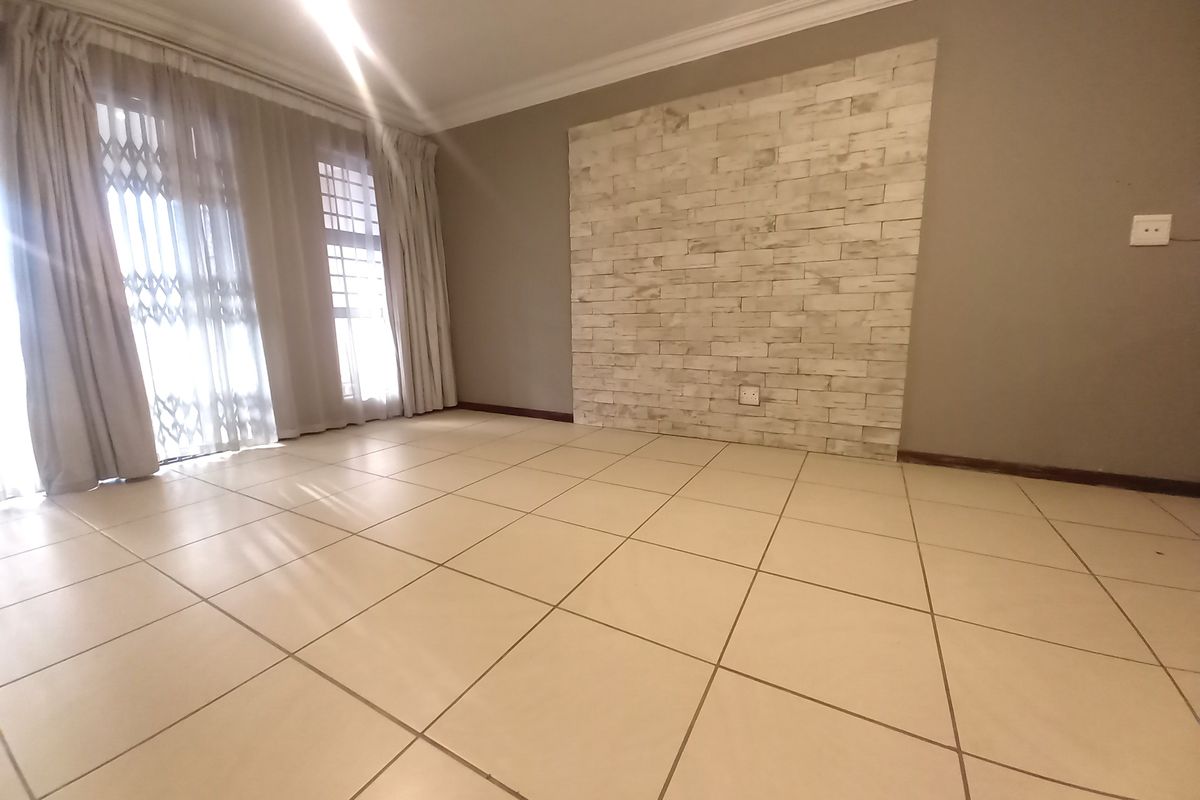 An empty living room featuring neutral tiled flooring, a decorative stone-look feature wall, and sliding glass doors with security gates leading to the exterior.