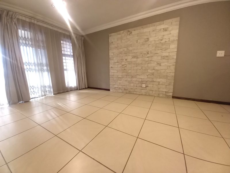 An empty living room featuring neutral tiled flooring, a decorative stone-look feature wall, and sliding glass doors with security gates leading to the exterior.