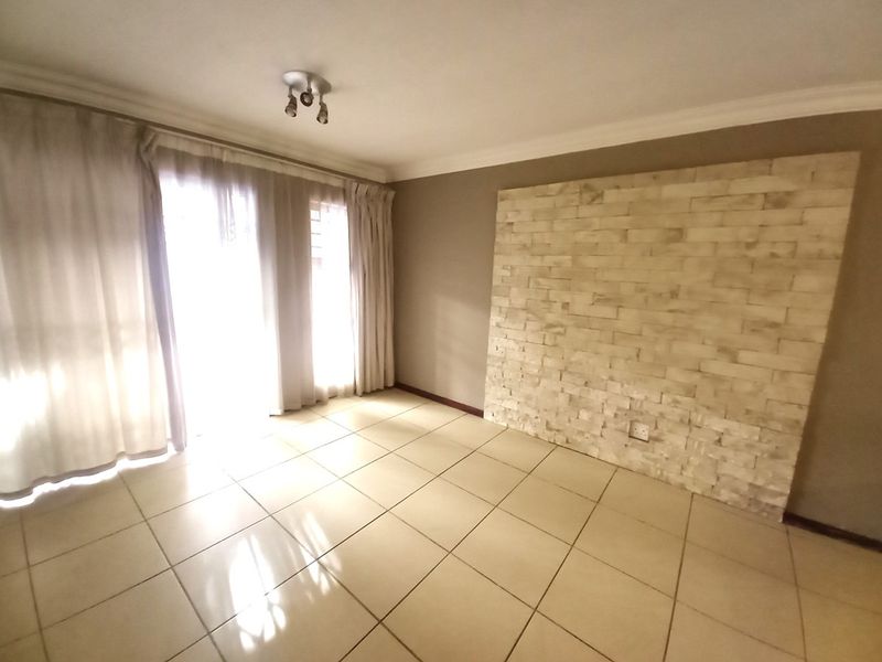 An empty living room featuring ceramic tile flooring, a decorative stone veneer feature wall, and modern track lighting.