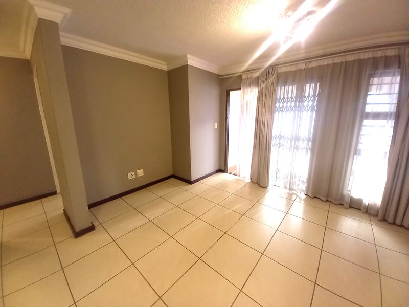 An empty living room featuring neutral wall paint, ceramic floor tiles, and a sliding glass door with a security gate leading to an outdoor area.