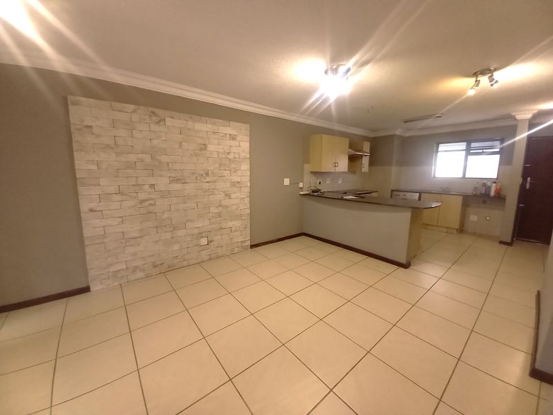 Open plan living and kitchen area featuring ceramic floor tiles, a stone veneer feature wall, and functional kitchen cabinetry with a breakfast bar.