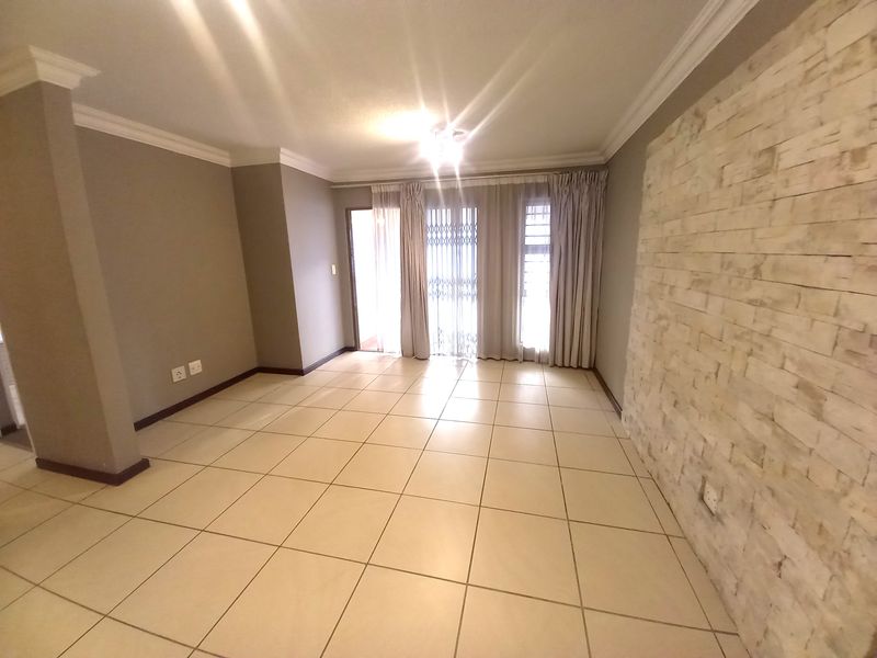 Spacious living area featuring neutral tiled flooring, a textured stone feature wall, and access to an outdoor balcony through sliding glass doors.