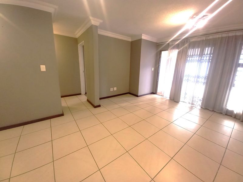 A bright, empty living room featuring neutral tiled flooring, decorative cornicing, and a sliding glass door providing access to an outdoor area.