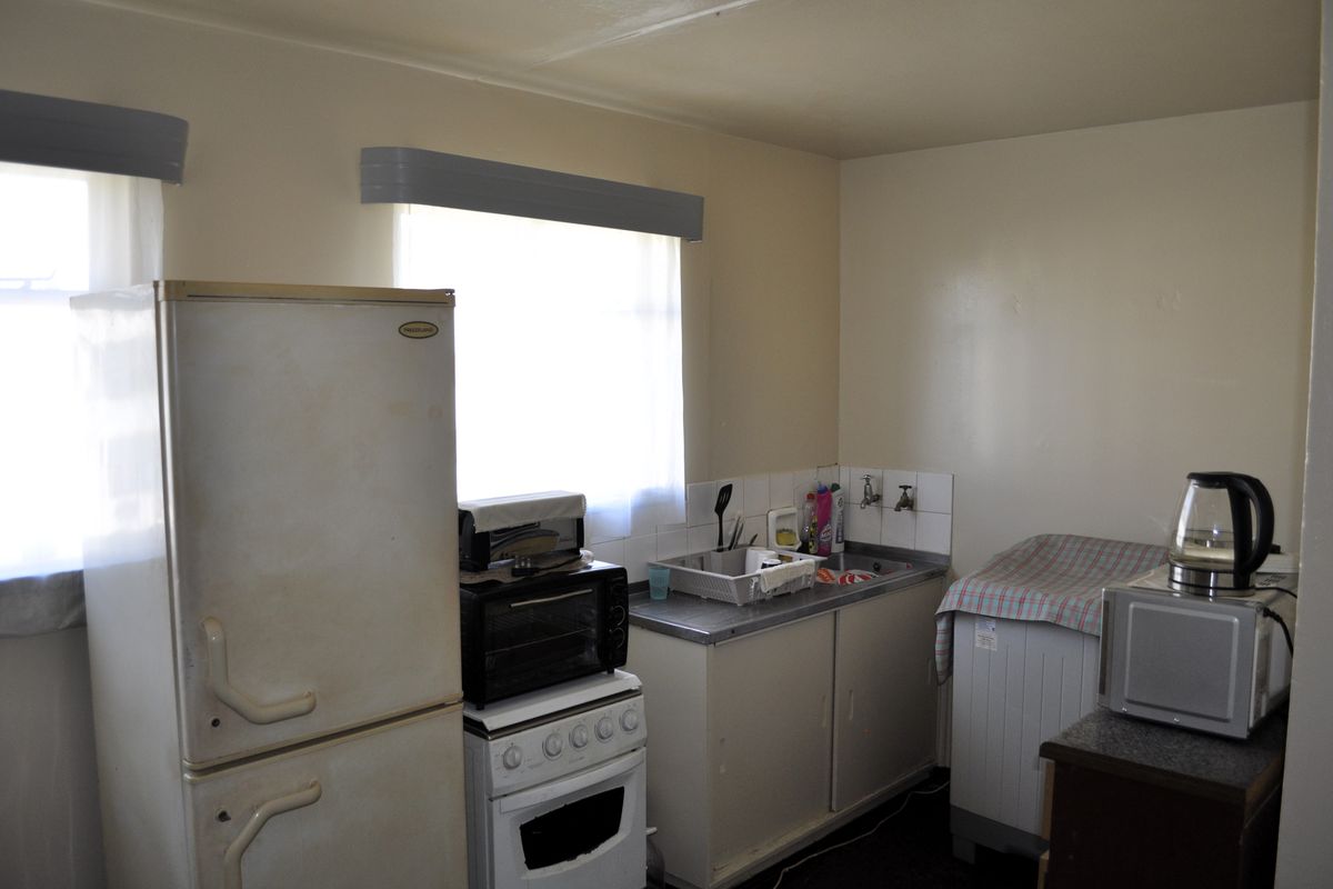 A functional kitchen area featuring a stainless steel sink, tiled splashback, and basic cabinetry, offering potential for modernization and renovation.