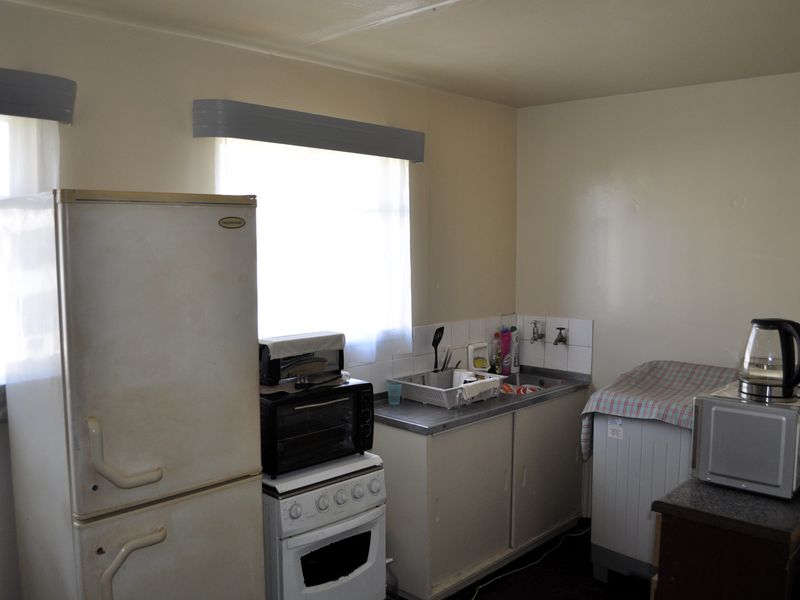 A functional kitchen area featuring a stainless steel sink, tiled splashback, and basic cabinetry, offering potential for modernization and renovation.