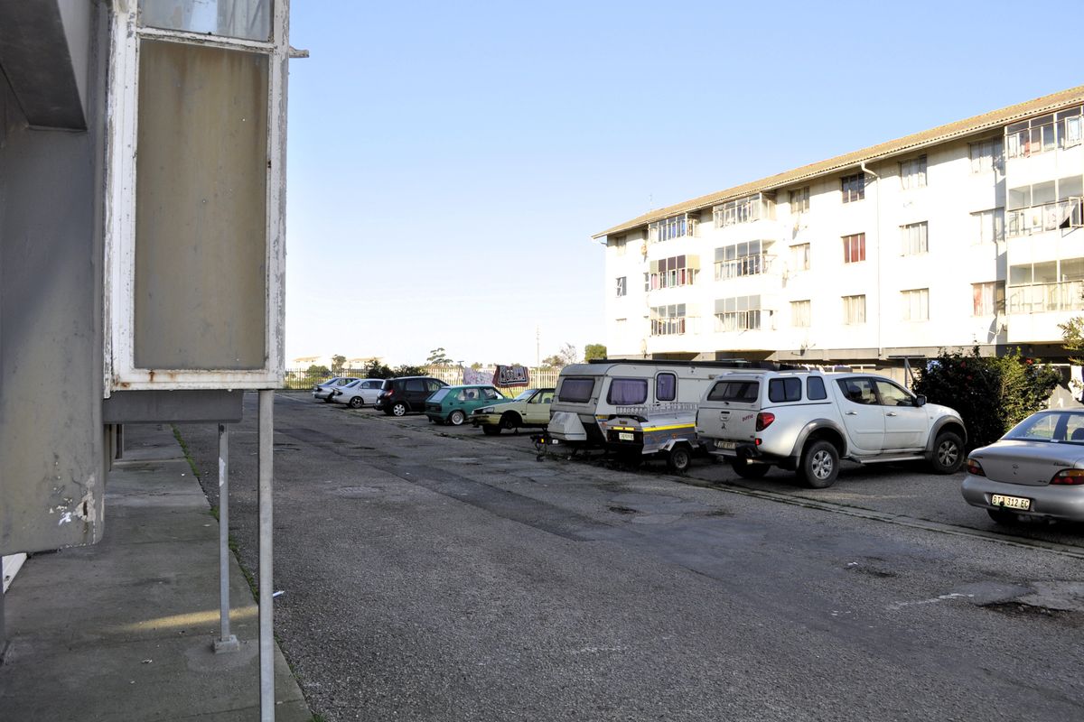 Exterior view of an apartment complex featuring an asphalt parking area and multi-story residential building with balconies.