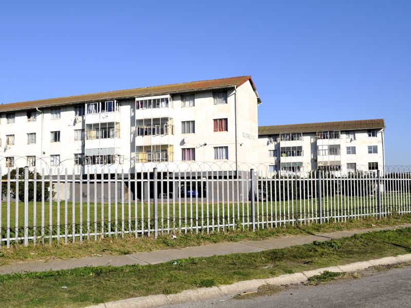 Exterior view of a multi-story apartment complex featuring security fencing, razor wire, and multiple balconies.