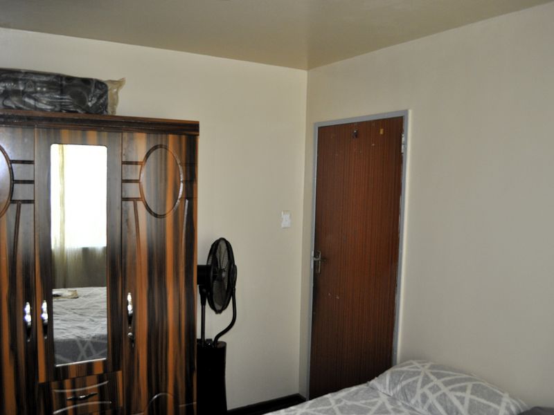 A bedroom interior featuring plain walls and a standard wooden door, requiring cosmetic updates to improve the overall aesthetic and finish.