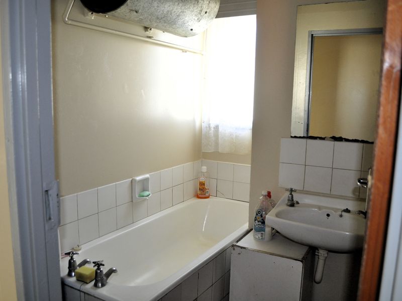 A dated bathroom featuring a standard bathtub, wall-mounted basin, and tiled splashbacks, requiring modernization to improve functionality and aesthetic appeal.