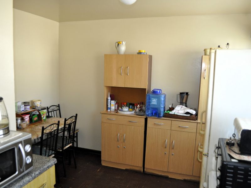 A compact kitchen area featuring light wood-tone cabinetry, laminate countertops, and dark vinyl flooring, offering a functional layout with potential for cosmetic updates.