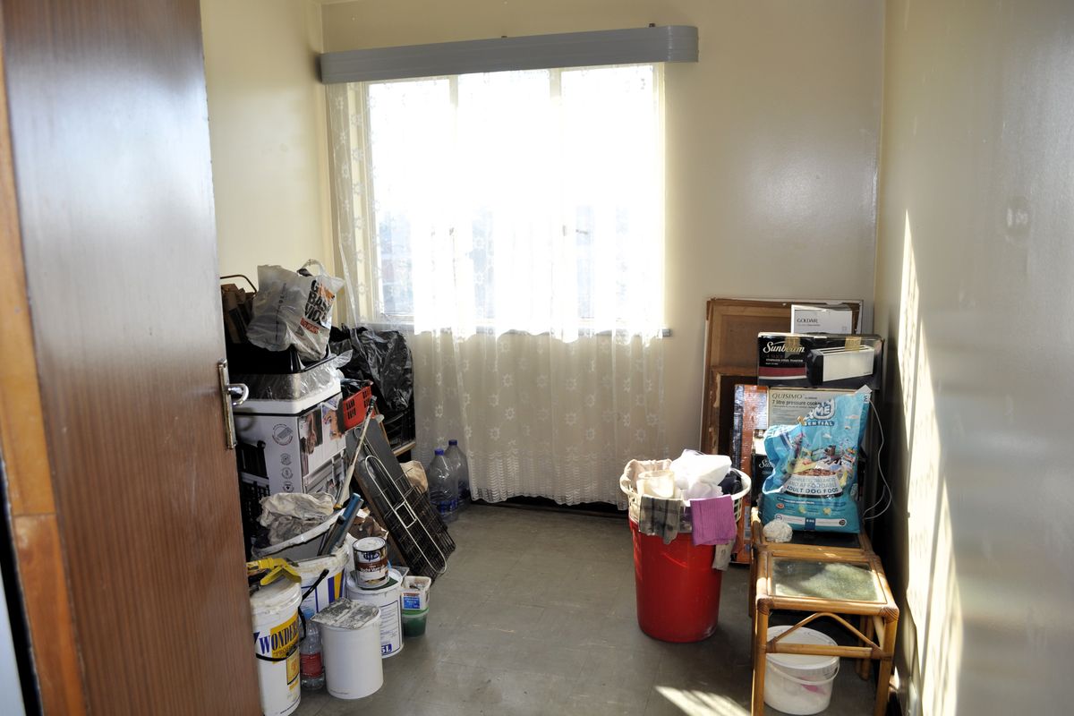 A small bedroom space featuring a window with a curtain rail, currently used for storage with worn wall and floor finishes.