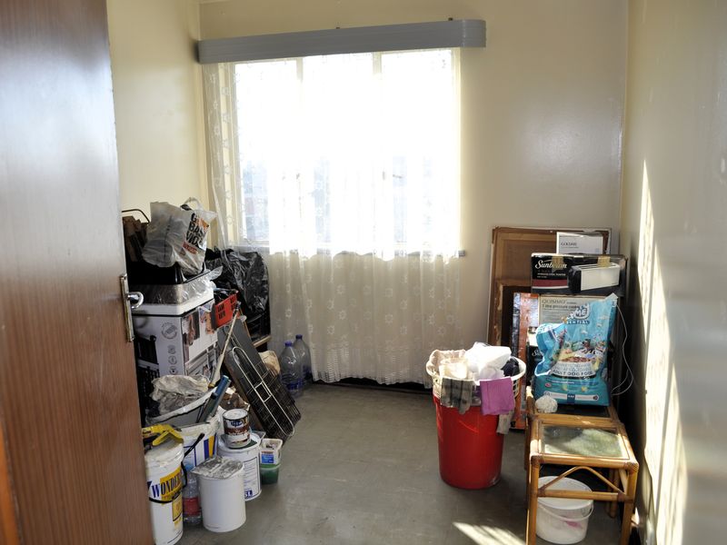 A small bedroom space featuring a window with a curtain rail, currently used for storage with worn wall and floor finishes.