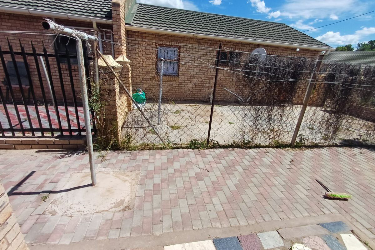 Rear exterior view of a brick house featuring a paved patio area, security fencing, and a washing line.