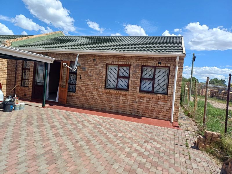 A well-maintained face brick house exterior featuring a tiled roof, secure window bars, and a paved driveway area.