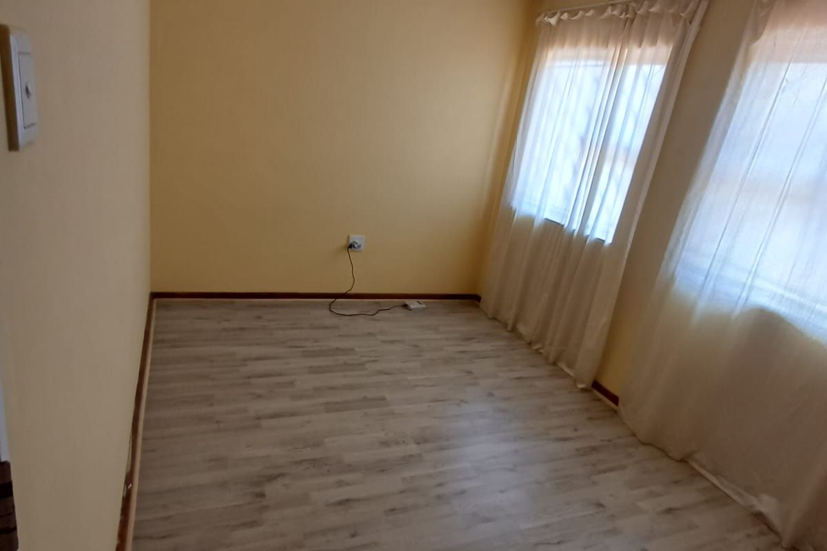 A bright, empty bedroom featuring light-toned laminate flooring, neutral yellow walls, and dual windows with installed curtain tracks.