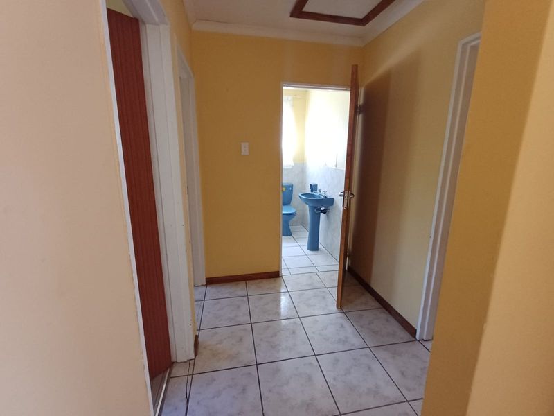 A tiled hallway providing access to a bathroom featuring dated blue sanitaryware.