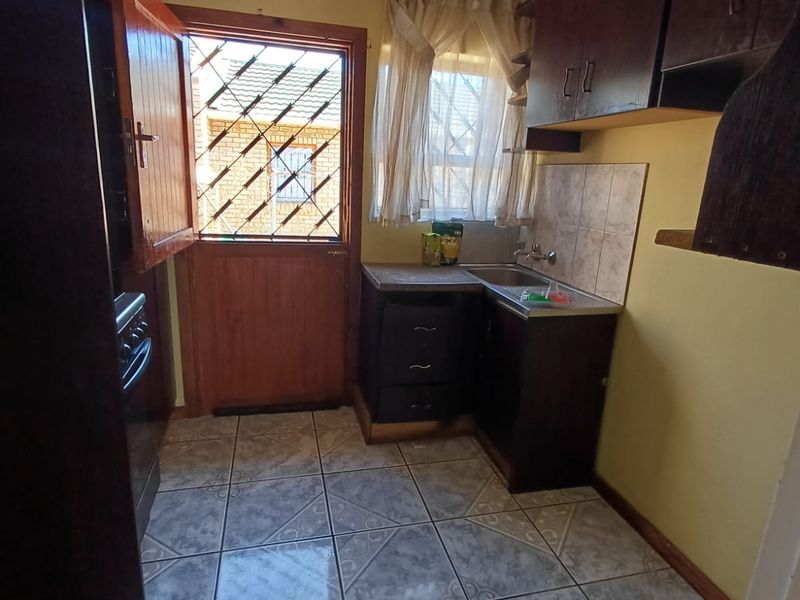 A compact scullery area featuring built-in dark cabinetry, a stainless steel sink, tiled flooring, and direct access to the exterior via a security door.