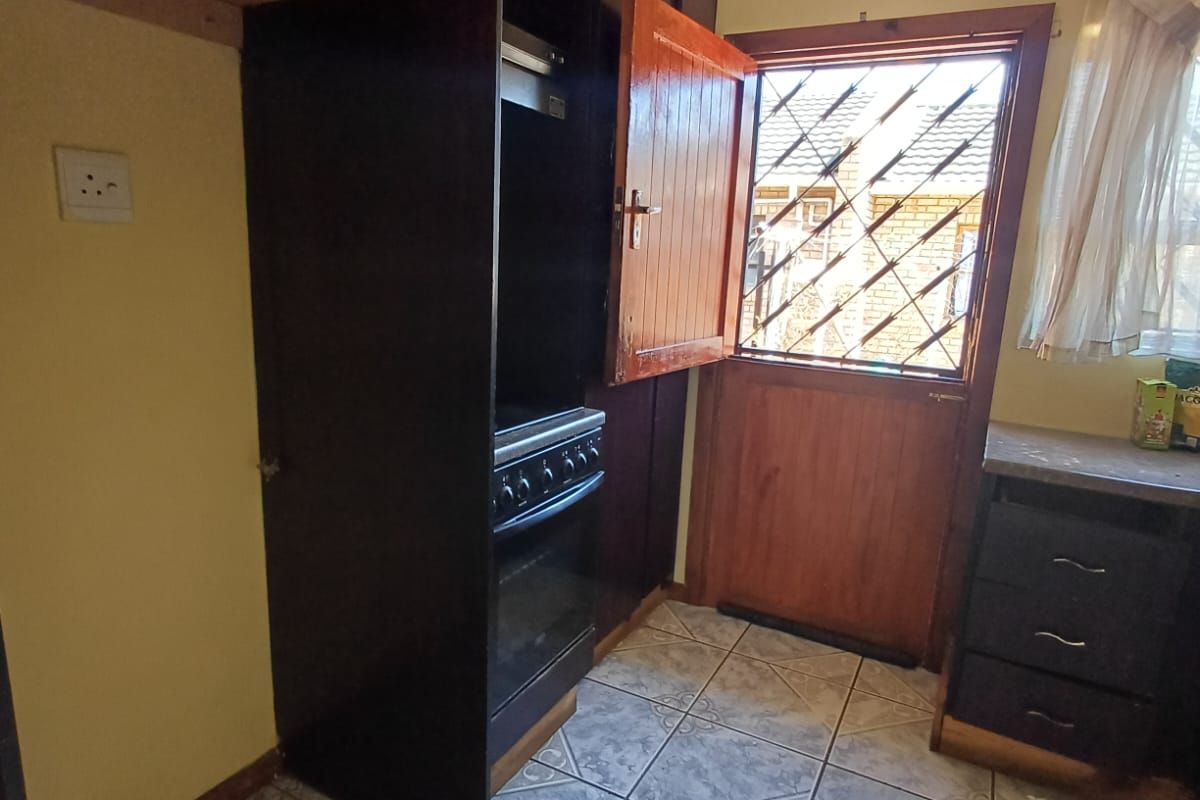 A functional kitchen featuring dark built-in cabinetry, a freestanding stove with extractor, tiled flooring, and direct access to the exterior via a security-gated door.