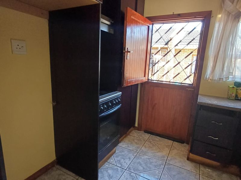 A functional kitchen featuring dark built-in cabinetry, a freestanding stove with extractor, tiled flooring, and direct access to the exterior via a security-gated door.
