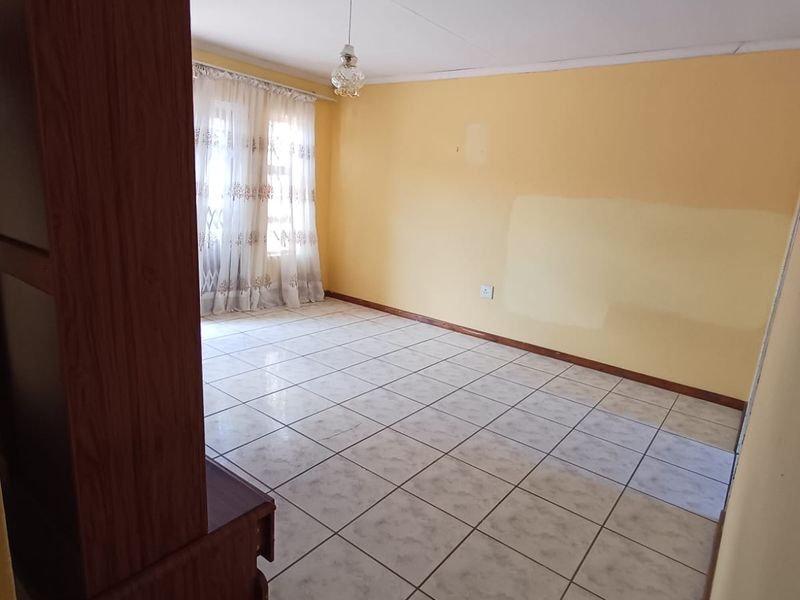 An empty living room featuring ceramic floor tiles and a pendant light fitting, with walls requiring cosmetic attention and repainting.