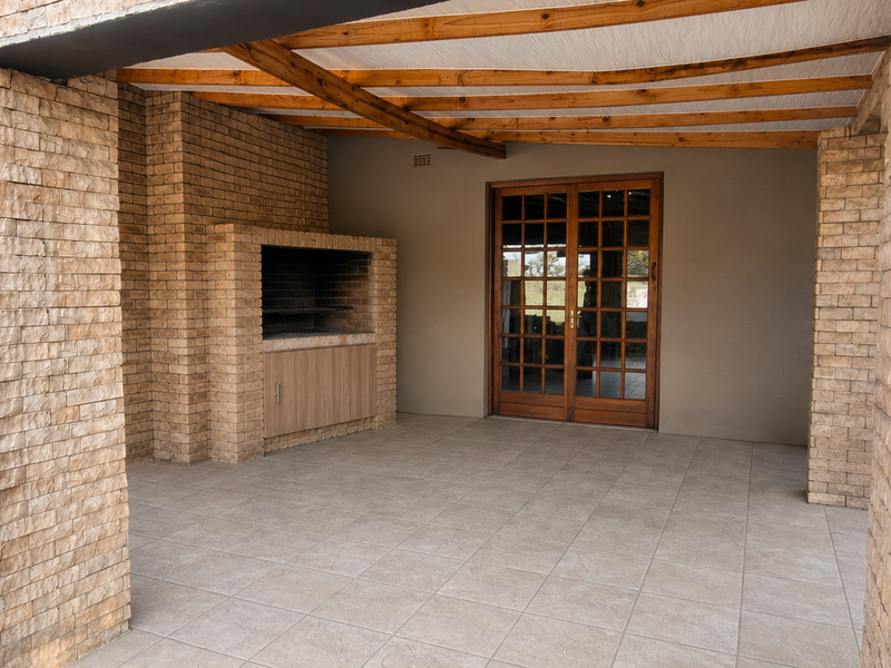 A spacious covered patio featuring a built-in brick braai, timber pergola ceiling, and tiled flooring, providing an ideal space for outdoor entertaining.