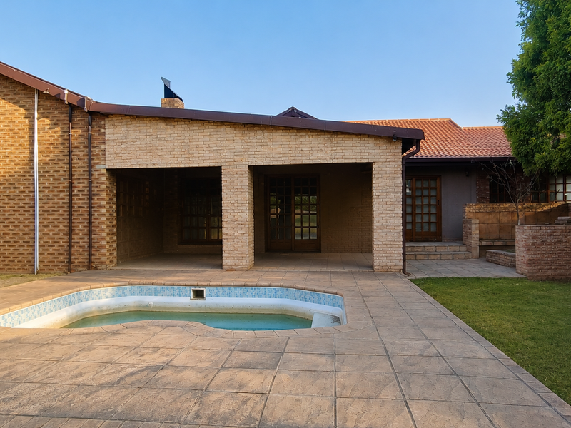 Rear exterior view featuring a covered patio, paved pool deck, and a swimming pool set within a landscaped garden area.