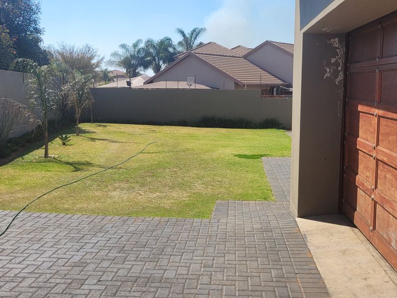 A rear exterior view featuring a paved driveway, a wooden garage door, and a private garden enclosed by a perimeter wall with electric fencing.