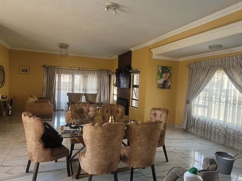 Spacious open-plan living and dining area featuring large windows, tiled flooring, and a central brick fireplace, offering a bright and versatile layout.