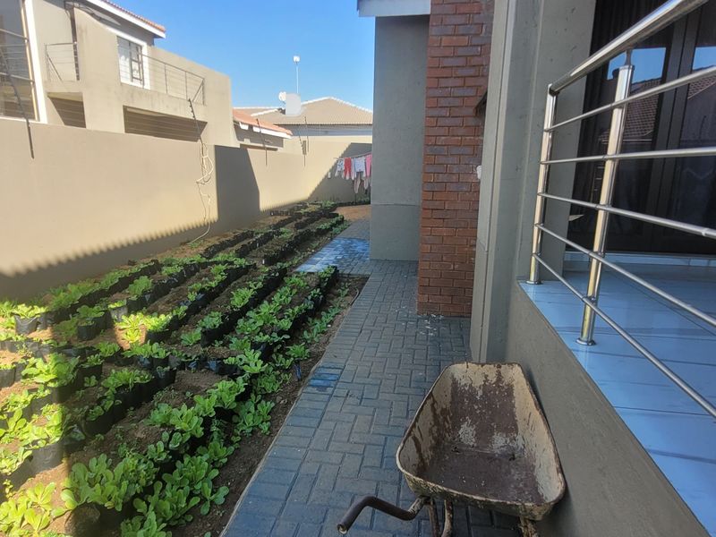 A side garden area featuring a paved walkway, brick pillar, and a tiled patio with a stainless steel balustrade.