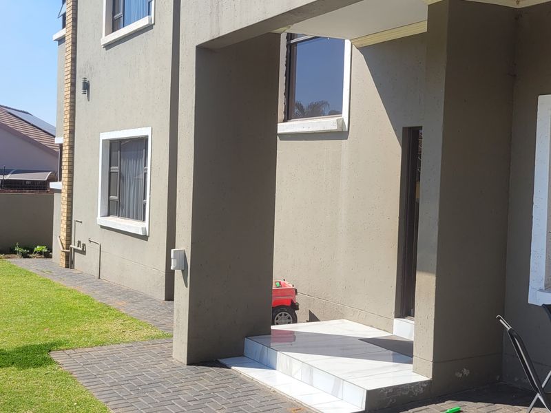 Rear exterior view of the property featuring a paved patio area, tiled entrance steps, and a well-maintained lawn with boundary walling.