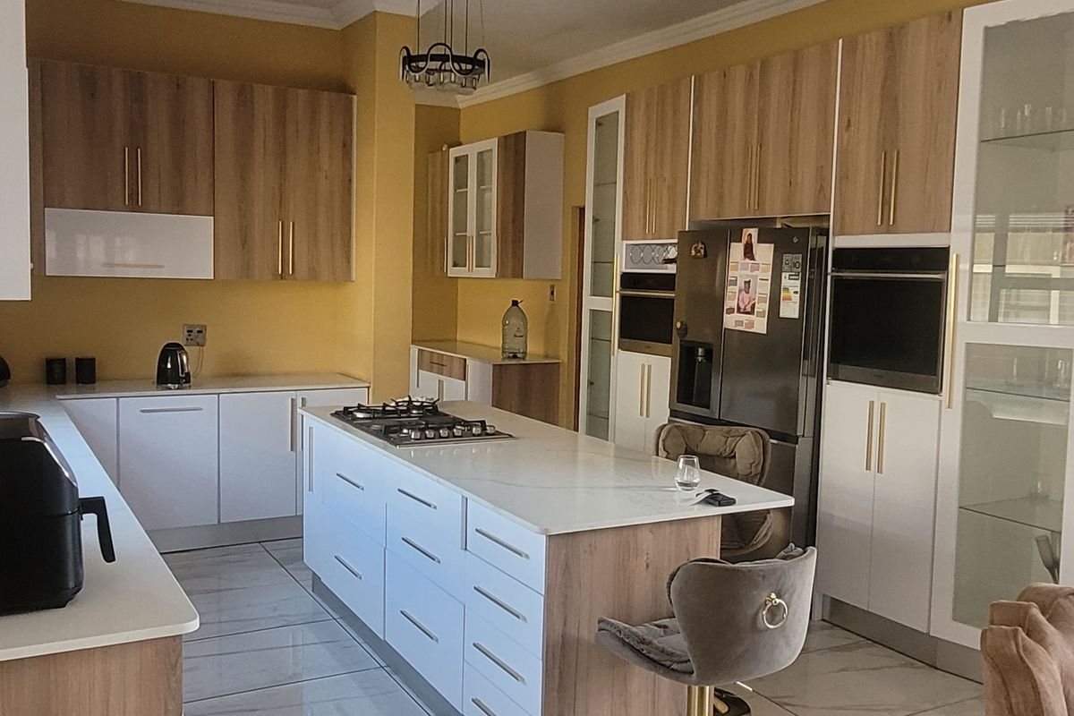 Modern kitchen featuring a central island with gas cooktop, stone countertops, integrated appliances, and ample cabinetry with a contemporary two-tone finish.