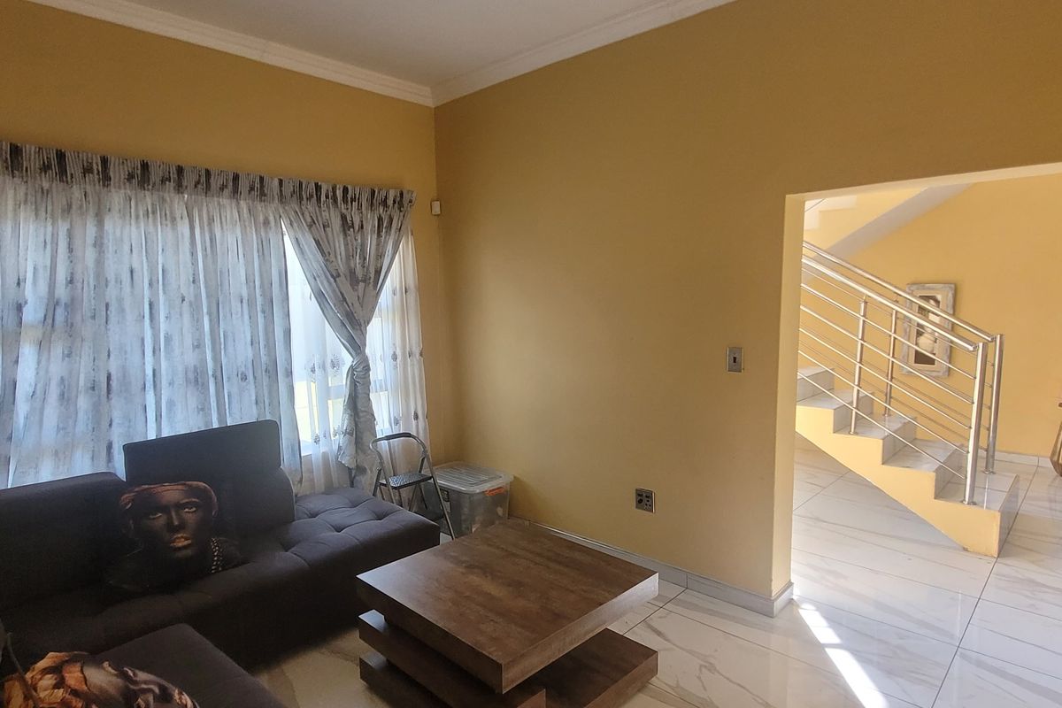 A living room area featuring tiled flooring and a staircase with a modern metal balustrade, leading to an adjacent hallway.