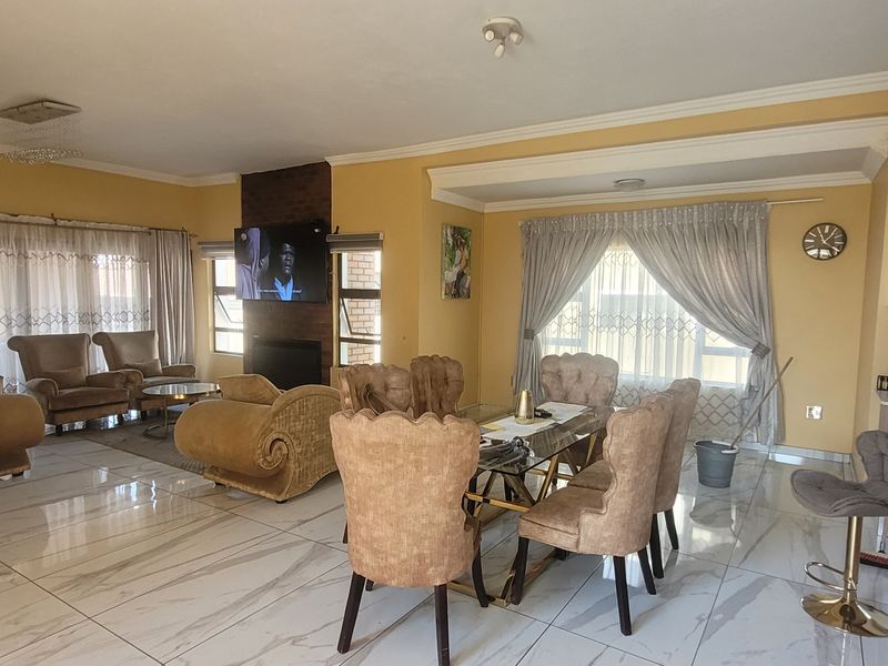 Spacious open-plan living and dining area featuring large format tiled flooring, a central fireplace, and neutral wall finishes.