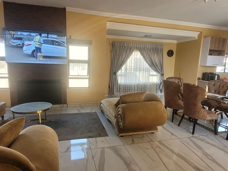 Spacious open-plan living and dining area featuring large format marble-look floor tiles, a built-in fireplace, and a modern kitchen with integrated cabinetry.