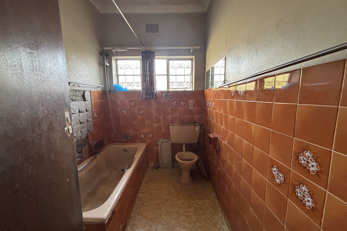 A dated bathroom featuring a bathtub, toilet, and orange ceramic wall tiles. The space requires renovation to update finishes and address wall damage.