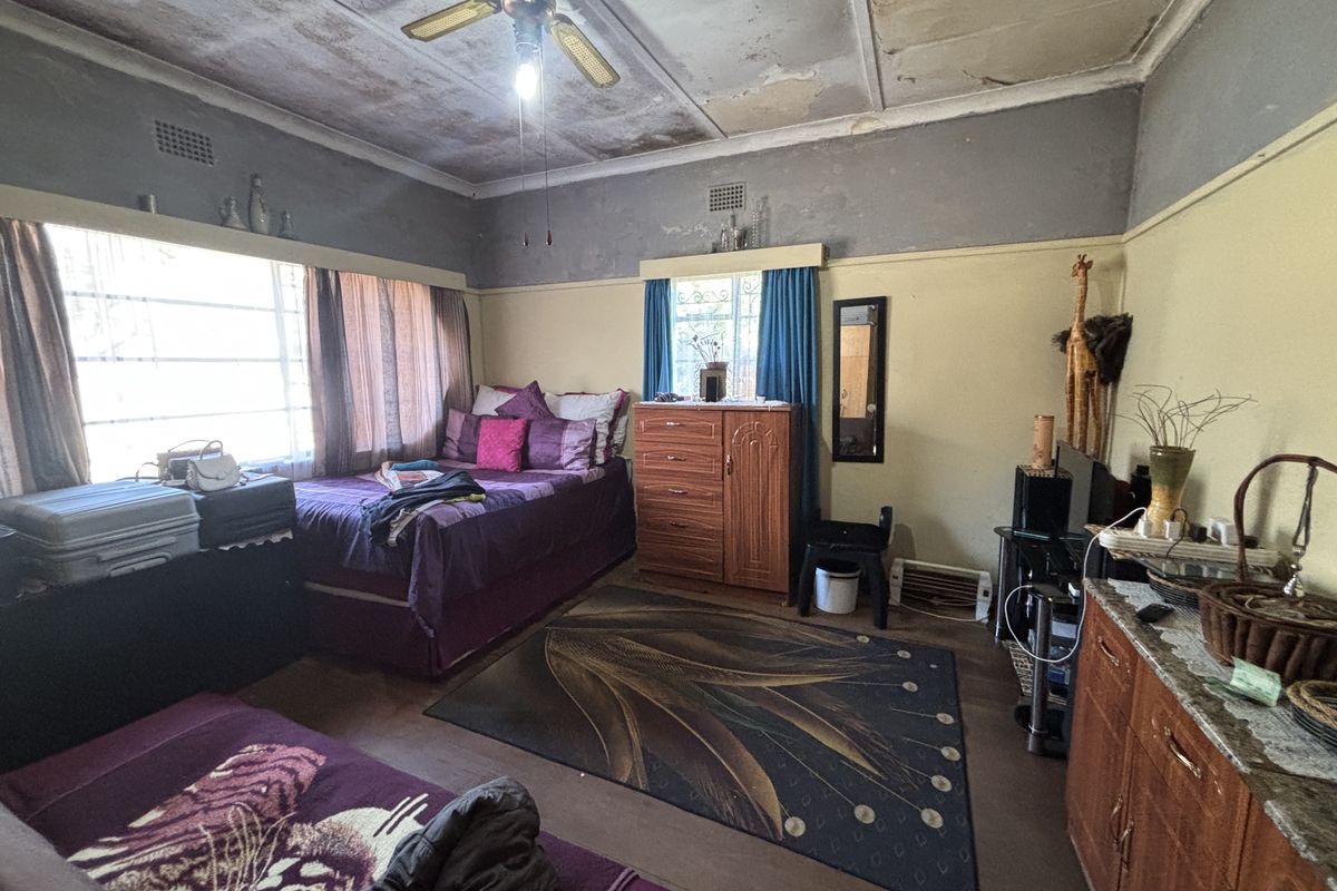 A bedroom featuring a ceiling fan and large windows, currently showing significant signs of wear including peeling paint and ceiling damage requiring renovation.