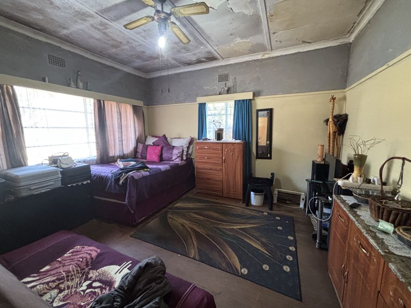 A bedroom featuring a ceiling fan and large windows, currently showing significant signs of wear including peeling paint and ceiling damage requiring renovation.