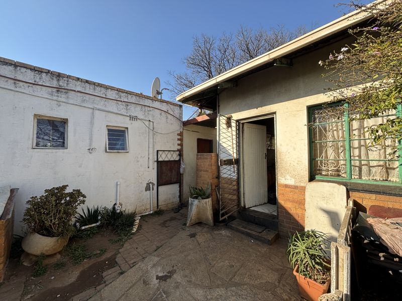 Rear exterior view of the property showing a paved courtyard area, security gates, and weathered brick and plaster wall finishes.