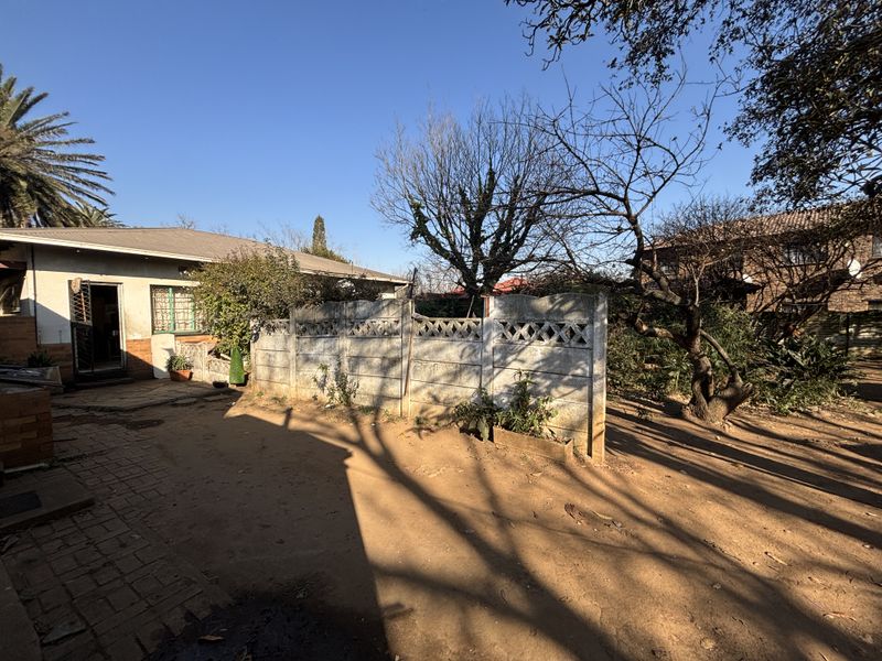 Rear exterior view of the property featuring a paved area, precast concrete boundary wall, and established garden trees.