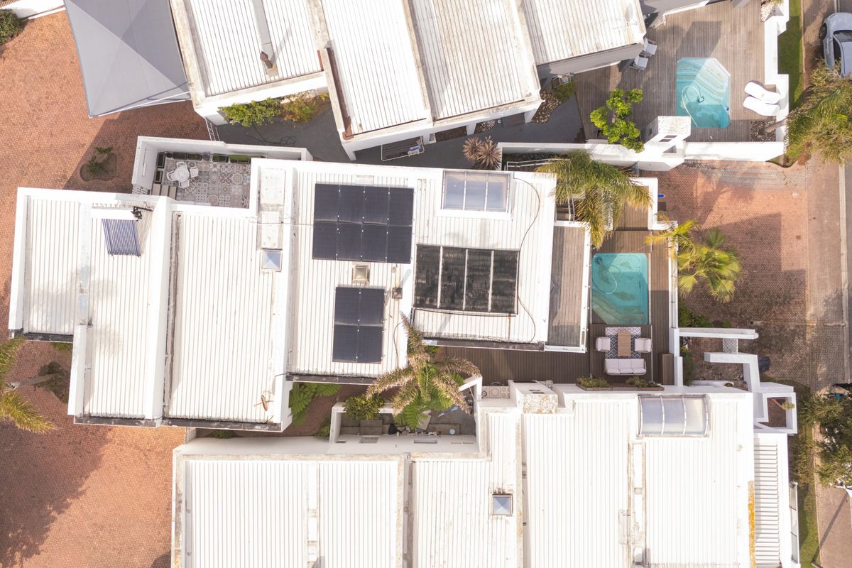 Aerial view of the property showcasing the roof layout, solar energy installations, swimming pool, and surrounding paved outdoor areas.