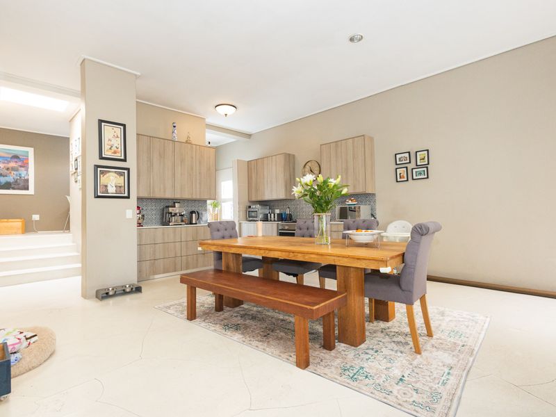 Open-plan living and dining area featuring modern wood-finish cabinetry, a tiled kitchen backsplash, and a staircase leading to an upper level.