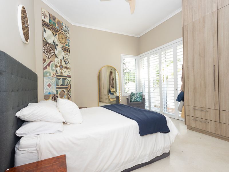 Spacious bedroom featuring built-in wardrobes, plantation shutters, and tiled flooring, offering direct access to the outdoor area.
