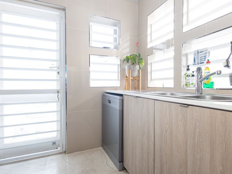 A functional laundry area featuring modern wood-look cabinetry, a stainless steel sink, and louvered windows providing natural light and ventilation.