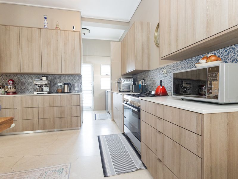 Modern kitchen featuring light wood-grain cabinetry, stone countertops, and a decorative patterned tile backsplash with integrated gas cooking appliances.