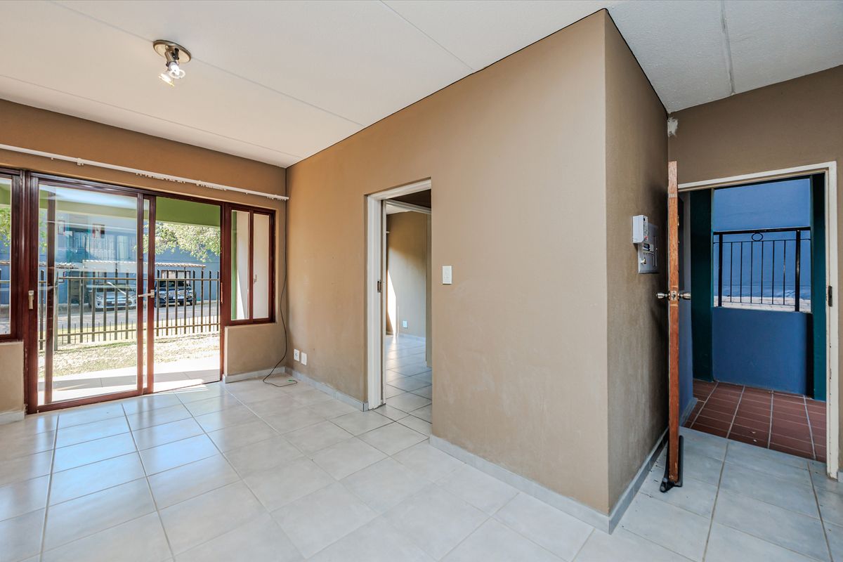 An empty living area featuring ceramic floor tiles, a sliding glass door leading outside, and an intercom system, requiring minor cosmetic updates.