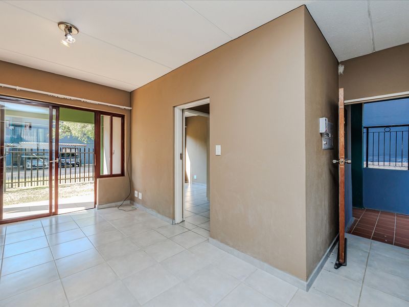 An empty living area featuring ceramic floor tiles, a sliding glass door leading outside, and an intercom system, requiring minor cosmetic updates.