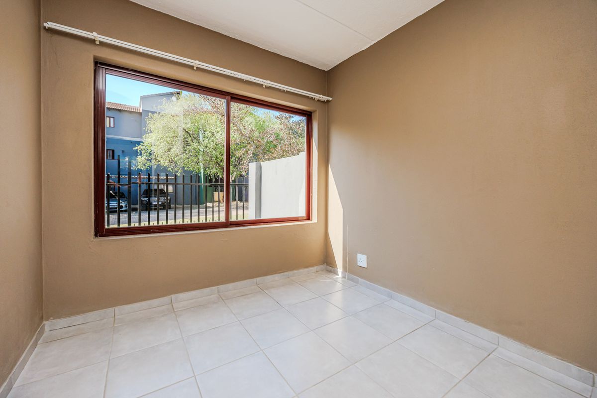 A bright, empty bedroom featuring neutral wall paint, tiled flooring, and a large sliding window with a curtain track.