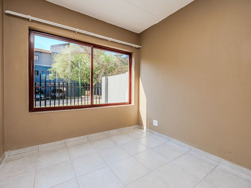 A bright, empty bedroom featuring neutral wall paint, tiled flooring, and a large sliding window with a curtain track.